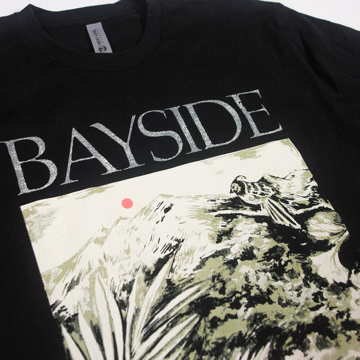 A black Bayside t-shirt displays BAYSIDE in bold white letters with a bird on rocks, mountains, plants, and a red sunโa unique design available only here.