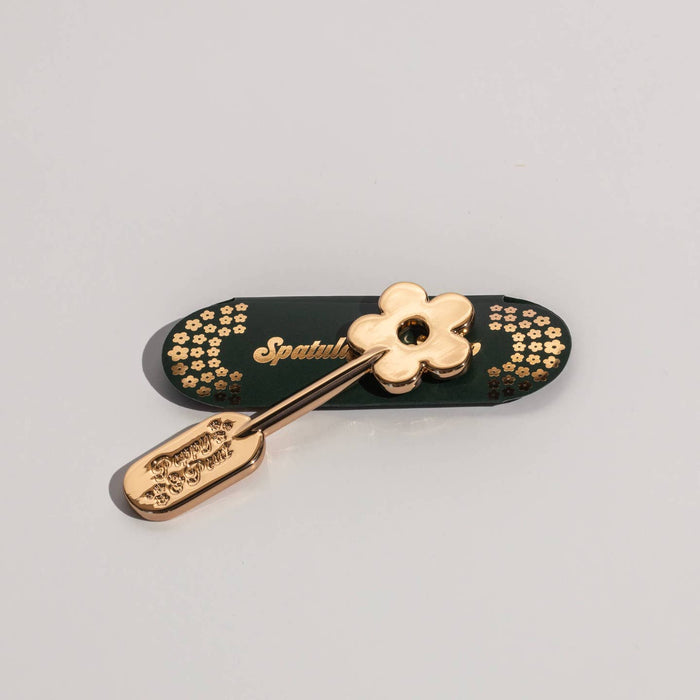 Gold lip care spatula with daisy-shaped handle and engraved floral pattern on the scoop