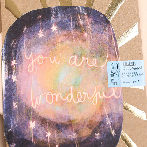 Close-up decorative greeting card front with โYou are wonderfulโ neon script on galaxy