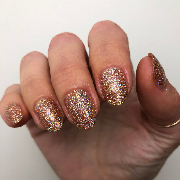 Hand with nails painted in Olive and June OBVI sparkling gold glitter polish showcasing a festive, long-lasting mani