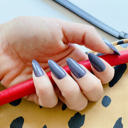 100% Chance - Press-On | Long | Almond showing hand with long almond press-on nails in moody gunmetal blue polish holding a patterned bag