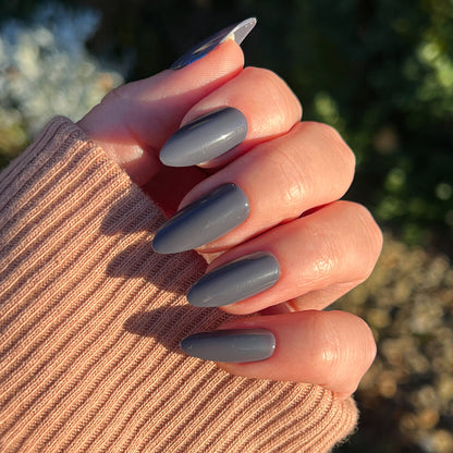 100% Chance - Press-On | Long | Almond showing hand with long almond press-on nails in moody gunmetal blue polish outdoors