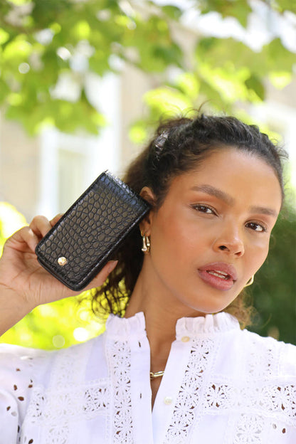 Female model holding Aisling Black crocodile print faux leather Lipstick Holder outside with a sunny background under a tree