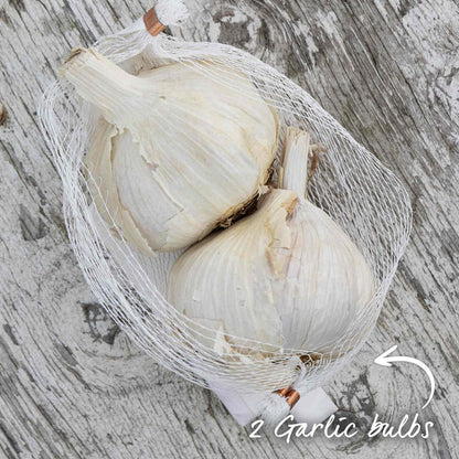 Two garlic bulbs in a mesh bag on a wooden surface.