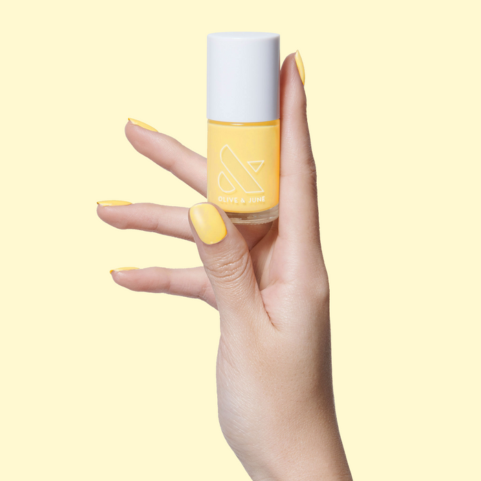 Hand holding Bright & Focused yellow nail polish with nails painted for a bright, cheerful at-home manicure look
