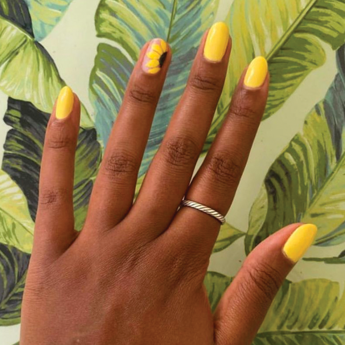Hand with Bright & Focused yellow gel polish and sunflower nail art for a cheerful at-home manicure by Olive and June