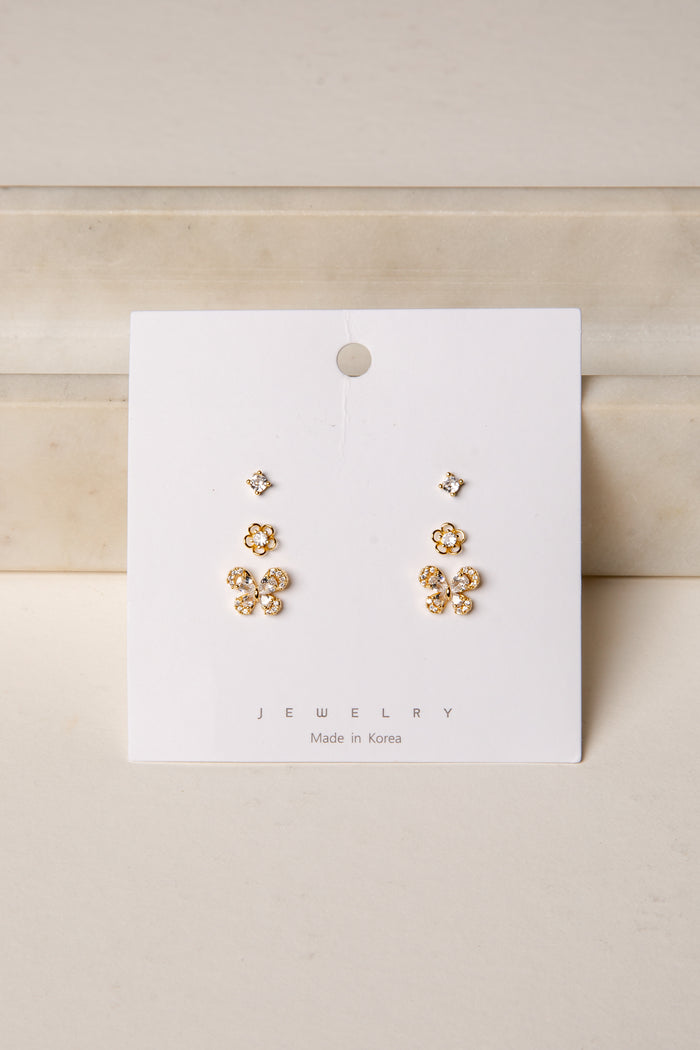 Gold floral earrings on a white card with 'Jewelry' label against a beige background