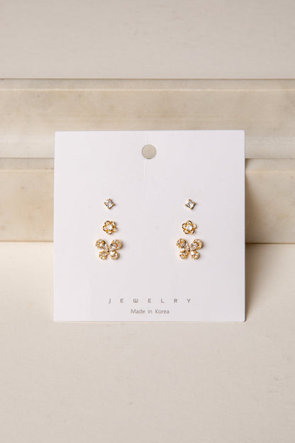 Gold floral earrings on a white card with 'Jewelry' label against a beige background