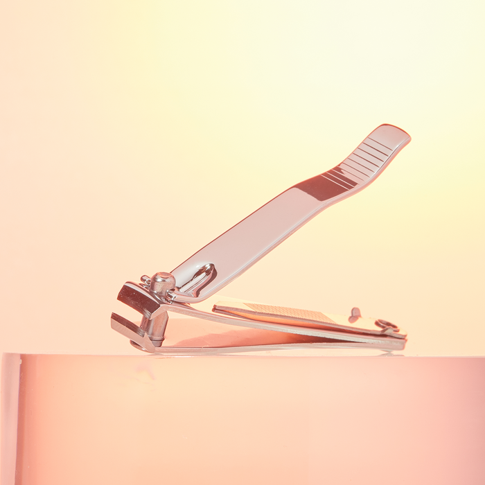 Stainless steel nail clipper open, standing on a peach background