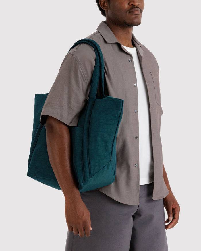 Teal tote bag held at side with two top handles and a structured front pocket.