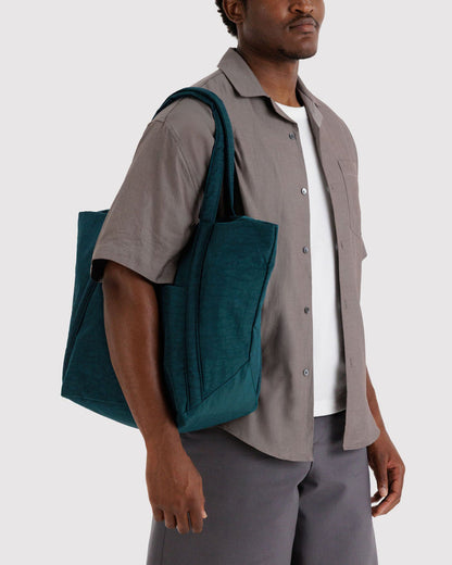 Teal tote bag held at side with two top handles and a structured front pocket.