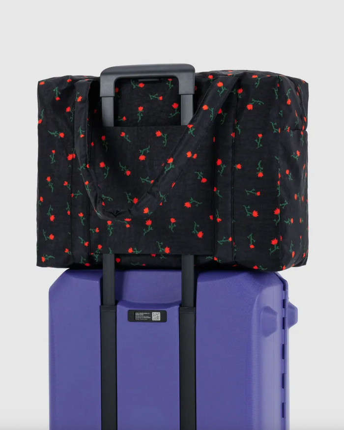 Cherry print carry-on bag with black exterior fitted over a rolling suitcase handle.