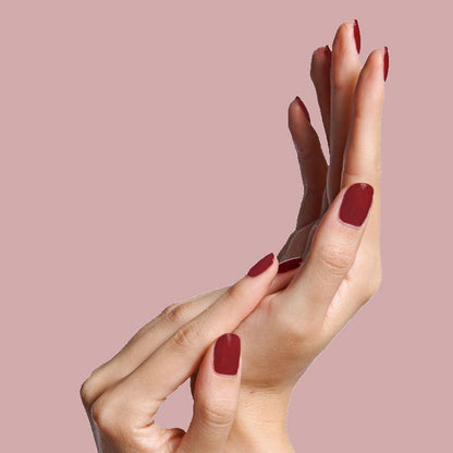 Hands with nails painted in warm brick red Cozy Up nail polish showing an elegant at-home manicure