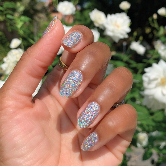 Hand with nails coated in Olive and June Exclamation Point silver holographic glitter polish for a sparkling mani outdoors