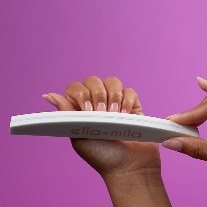Buffing nails with the white half-moon file buffer on a purple background