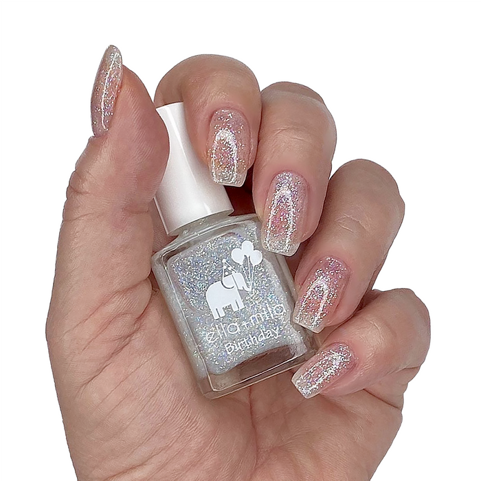 First Birthday iridescent micro glitter nail polish on a medium skin tone, hand holding the bottle