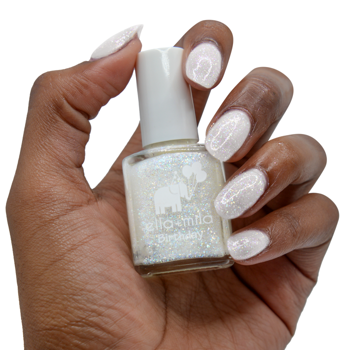 First Birthday iridescent micro glitter nail polish on a deep skin tone, hand holding the bottle