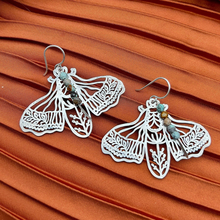 Handmade Peppered Moth earrings by Fluff Hardware featuring detailed black and white moth designs on silver hooks.