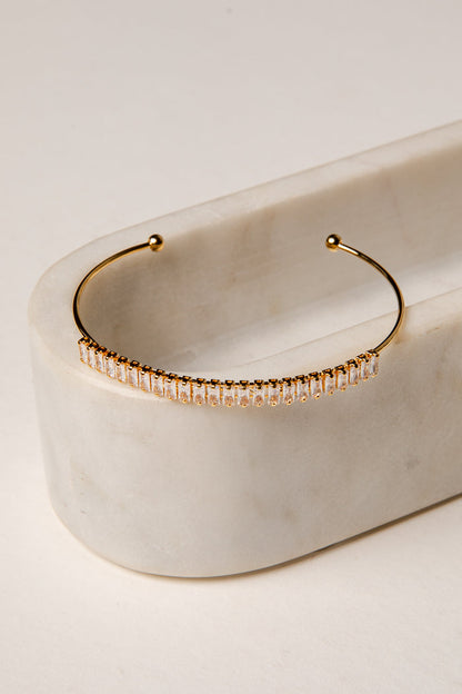 Gold hoop earring with embedded stones on a marble surface