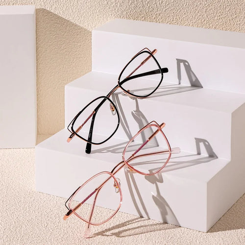 Two pairs of EyeCandys Kaylee Cat Eye glasses, one in black and one in rose gold, are shown on white geometric steps against a textured beige background, with soft shadows highlighting these fashionable eyeglasses.