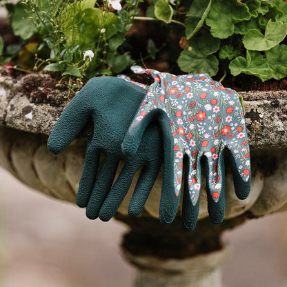 Pair of gardening gloves, one green and one with floral pattern, on a stone surface with plants in the background.