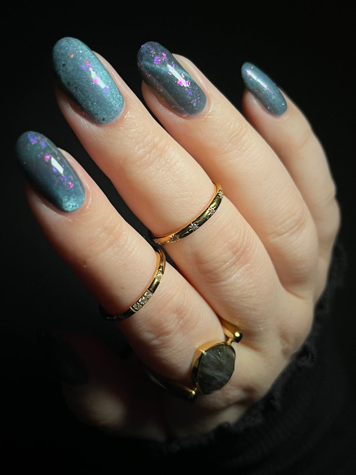 Hand with dusky gray blue magnetic nail polish with pink flakes. Opal Theory Polish Lagoon Nebula