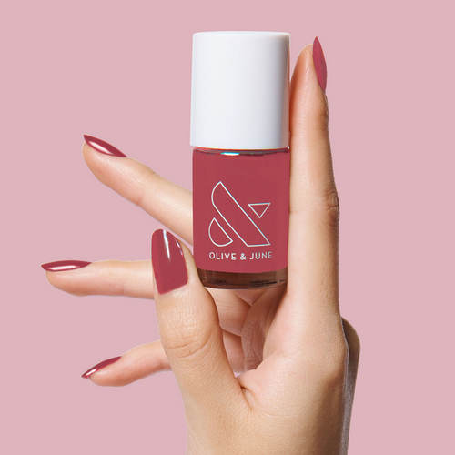 Hand holding Olive and June LD nail polish bottle with nails painted in a rosy pink shade for a polished mani look