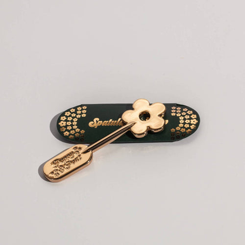 Gold lip care spatula with daisy-shaped handle and engraved floral pattern on the scoop