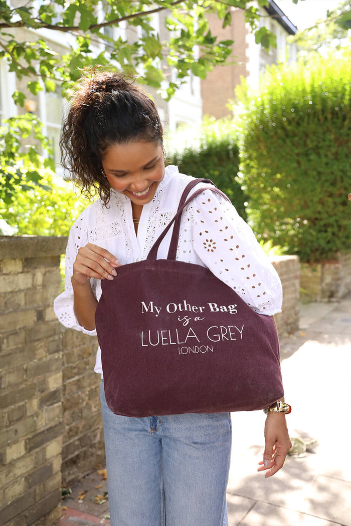 Model wearing Luella Cherry Canvas Shopper with printed white writing details over her shoulder with the two shoulder straps