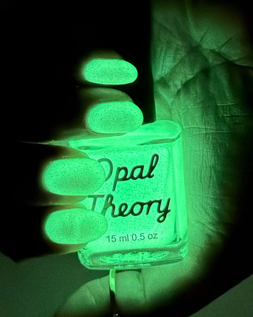Opal Theory nail polish bottle glowing green in a dark setting
