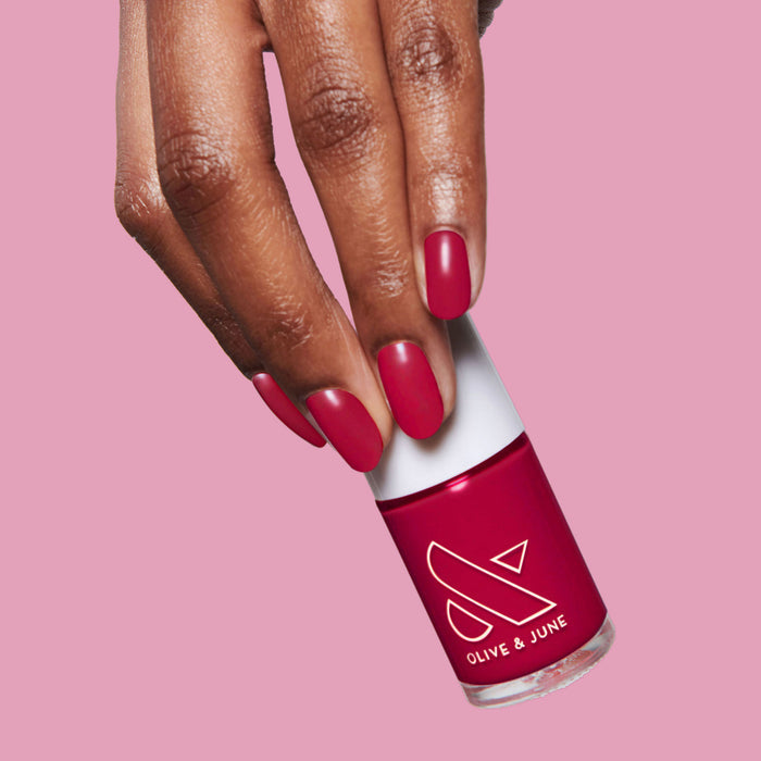 Hand holding Nailfie Time nail polish bottle with nails painted in rich ruby red for a classic mani look