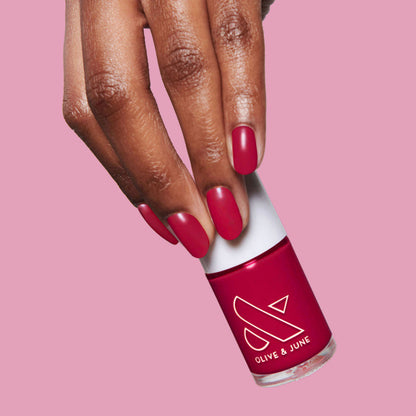 Hand holding Nailfie Time nail polish bottle with nails painted in rich ruby red for a classic mani look