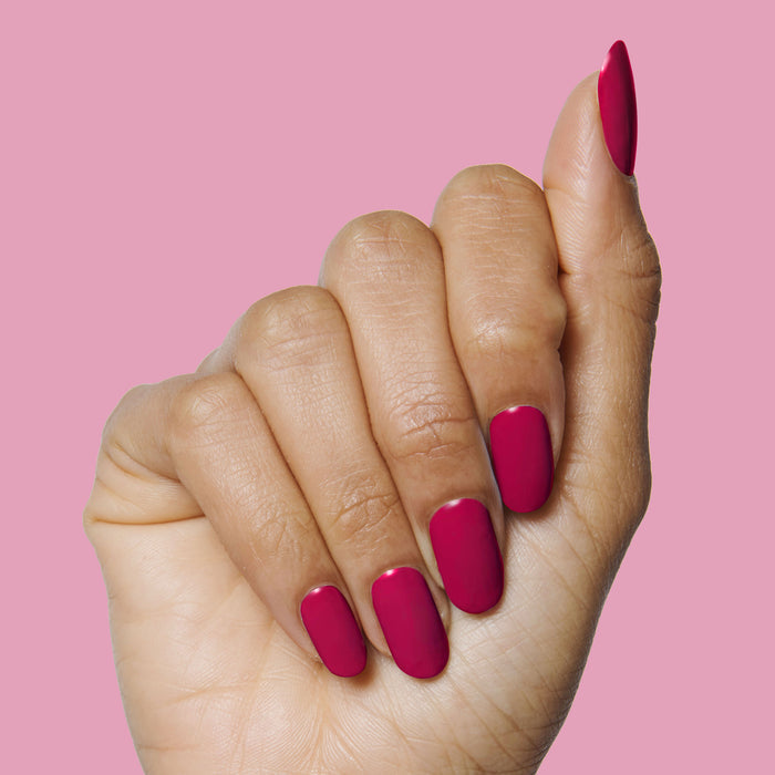 Hand showing nails painted in jewel-toned red Nailfie Time polish on pink background for a polished manicure look