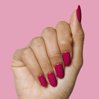 Hand showing nails painted in jewel-toned red Nailfie Time polish on pink background for a polished manicure look