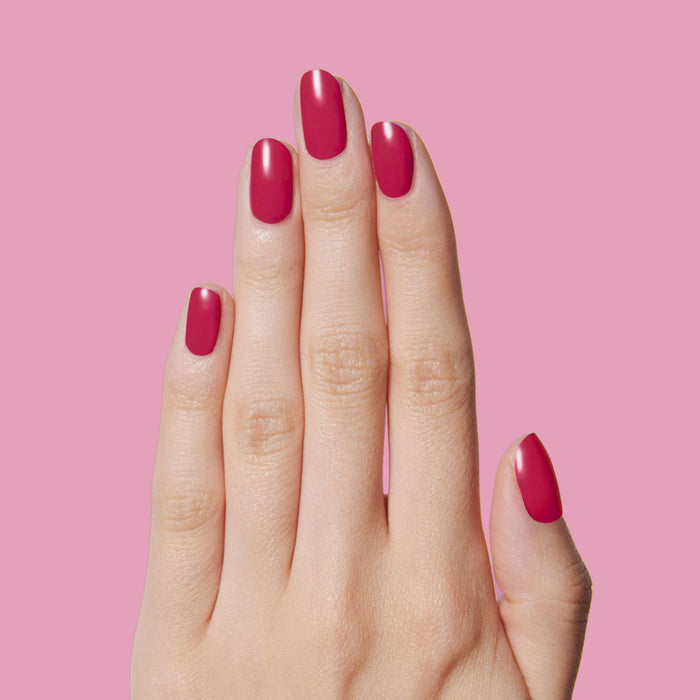Hand with nails painted in deep ruby red using Nailfie Time polish for a smooth, long-lasting manicure on pink background