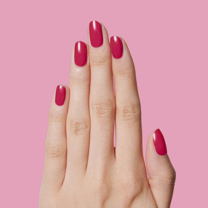 Hand with nails painted in deep ruby red using Nailfie Time polish for a smooth, long-lasting manicure on pink background