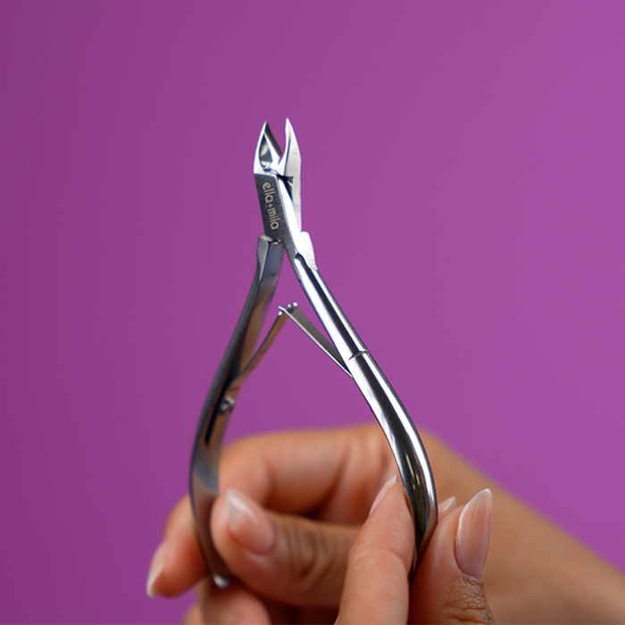 Hand holding the stainless steel cuticle nipper on a purple background