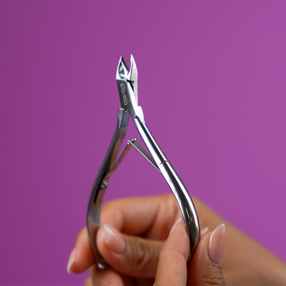 Hand holding the stainless steel cuticle nipper on a purple background