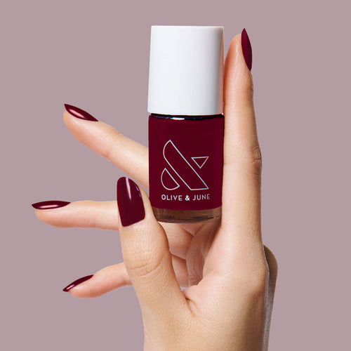 Hand with nails painted in dark ruby using Obsessed polish by Olive & June for a smooth, long-lasting mani