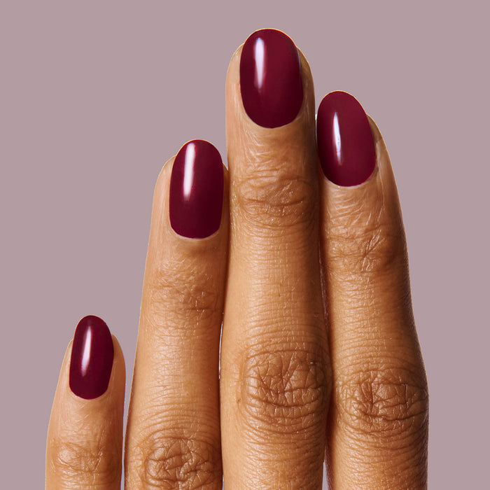 Hand with nails painted in rich dark ruby red using Obsessed polish for a smooth, long-lasting manicure look