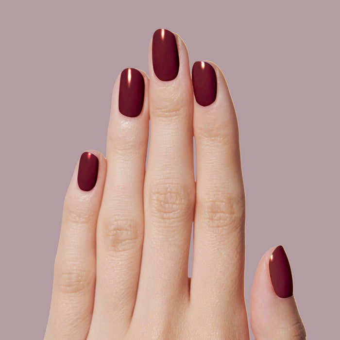Hand with nails painted in dark ruby red using Obsessed polish for a smooth, long-lasting manicure look