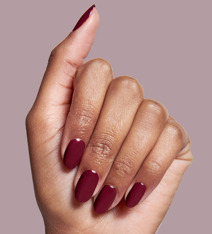 Hand with nails painted in deep rich red using Obsessed polish for a smooth, long-lasting manicure look