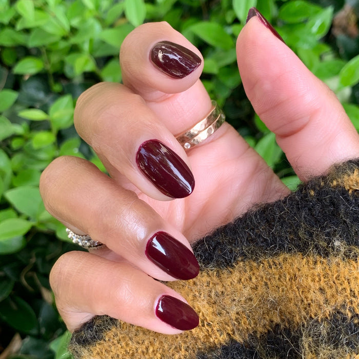 Hand with nails painted in rich dark ruby using Obsessed polish for a smooth, long-lasting manicure by Olive and June