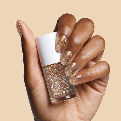 Hand showing nails painted with OBVI gold glitter polish holding the bottle for a festive at-home manicure