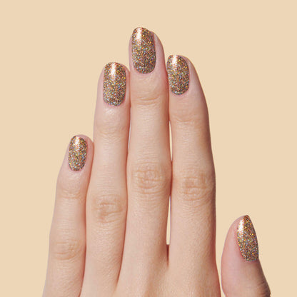 Hand showing nails painted with OBVI gold glitter polish for a festive and long-lasting at-home manicure