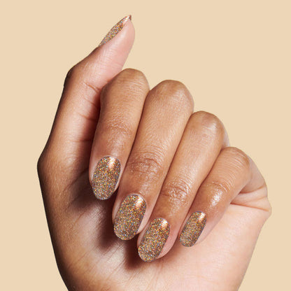 Hand with nails painted in OBVI sparkling gold glitter polish for a shimmering at-home manicure look