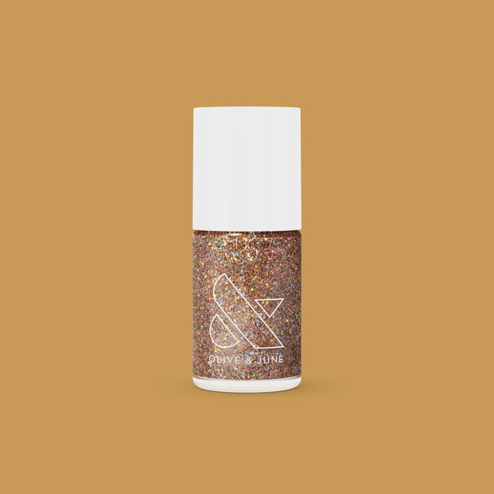 Olive and June OBVI gold glitter polish bottle on tan background for a sparkling, long-lasting mani or at-home manicure