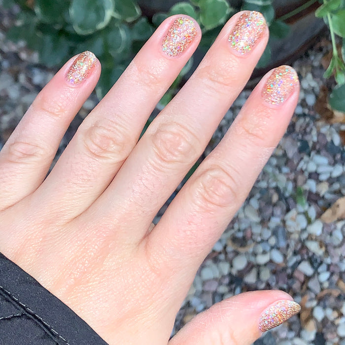 Hand with nails coated in Olive and June OBVI sparkling gold glitter polish for a bright, festive at-home manicure