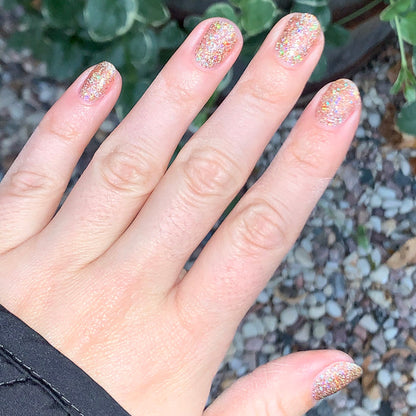 Hand with nails coated in Olive and June OBVI sparkling gold glitter polish for a bright, festive at-home manicure