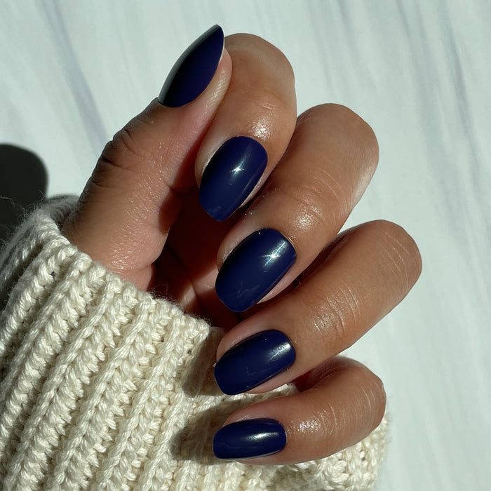 OMG - Press-On | Short | Round showing hand with glossy deep indigo short round press-on nails against light background